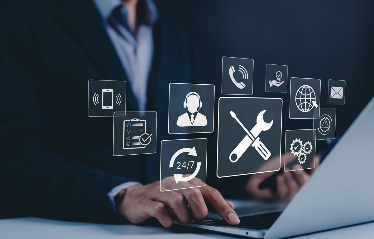 A technician in a suit types on a laptop with floating support icons — phone, headset, 24/7, wrench, checklist, mail, globe — representing technical support and 24/7 customer service