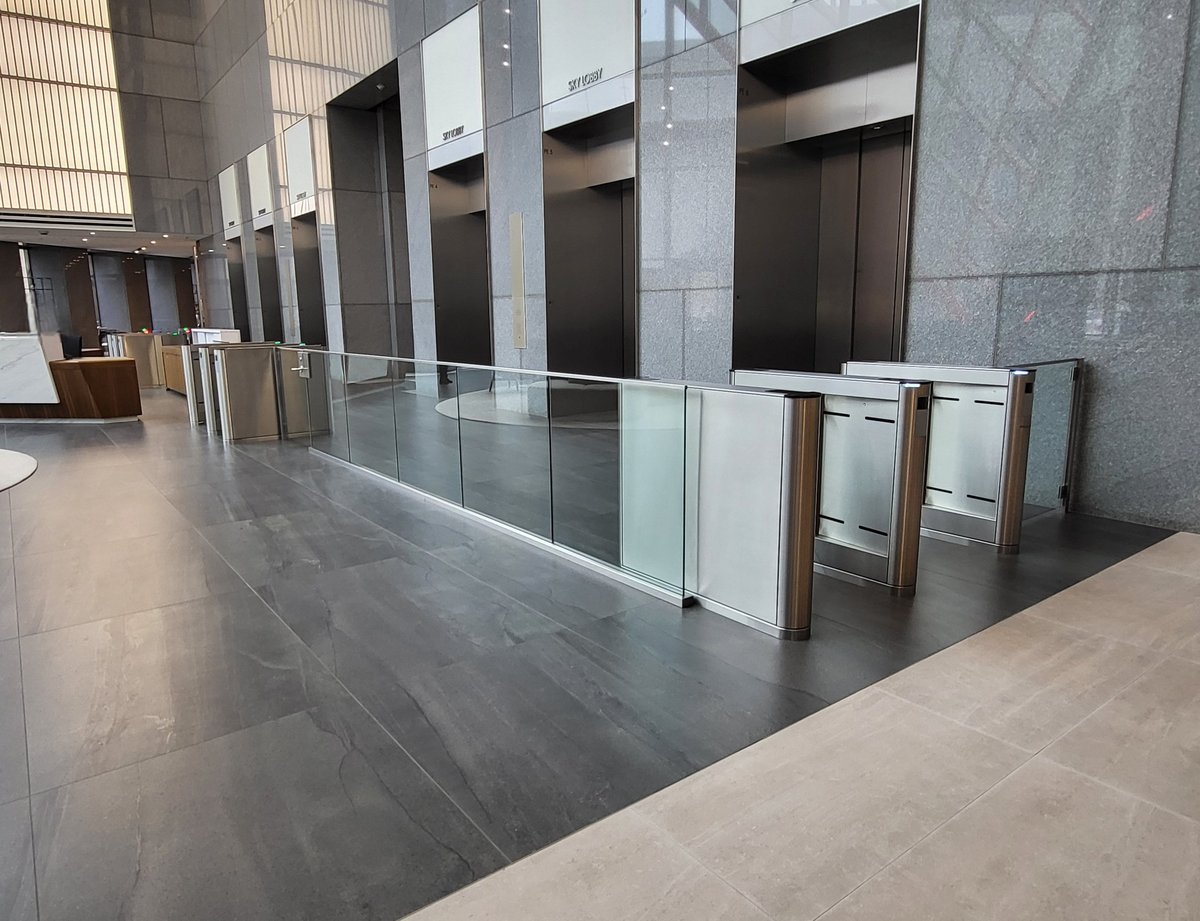 Modern building lobby with polished floor, glass railing, elevator doors, and concrete columns