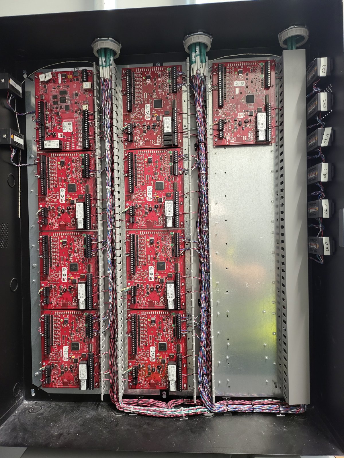 Industrial control panel with stacked red circuit boards, cooling towers, and bundled wiring inside black enclosure