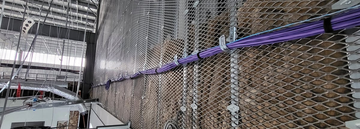 Bundled purple low-voltage cabling routed along expanded-metal mesh in an industrial interior