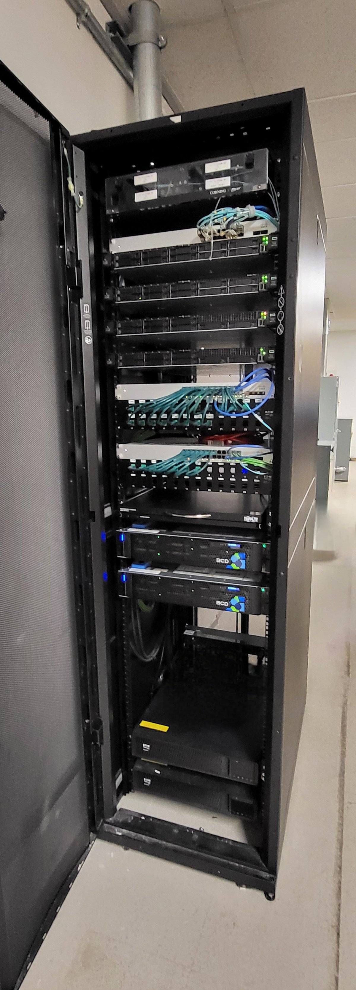 Black wall-mount server rack with network equipment, patch panels, and blue and green cables organized inside